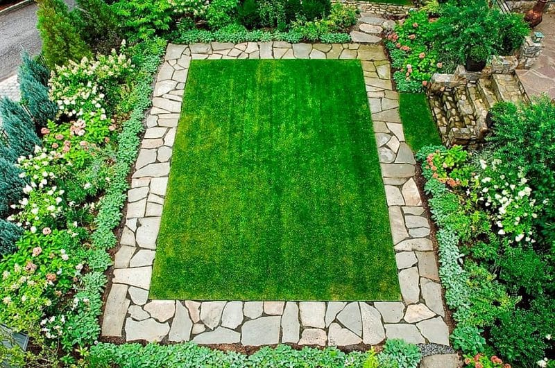 irregular flagstone lawn edging with shrub border complementing the lawn and smaller flagstone stair steps with weathered green lantern on stair’s stone veneer post and hammered copper chiminea on upper stone patio