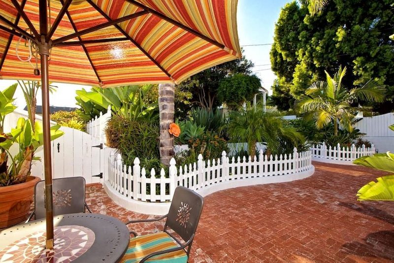 white curved gothic picket fences with round patio table with umbrella and gray metal patio chairs with damask cutout backrest and aged brick floor in herringbone pattern