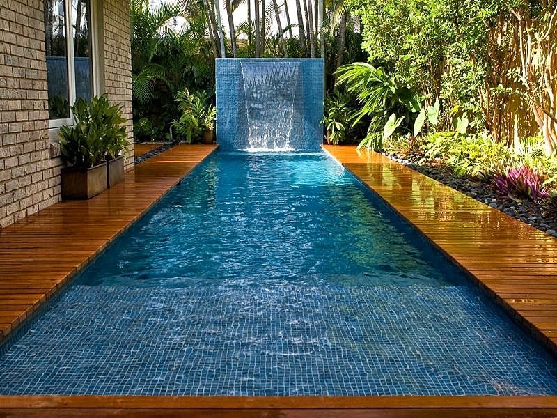 lap pool with sheer descent waterfall wall feature and blue blend swimming mosaic tiles on pool sun shelf with teak hardwood pool decking and river rock as garden mulch and deck inlay with cube corten steel planter boxes on poolside